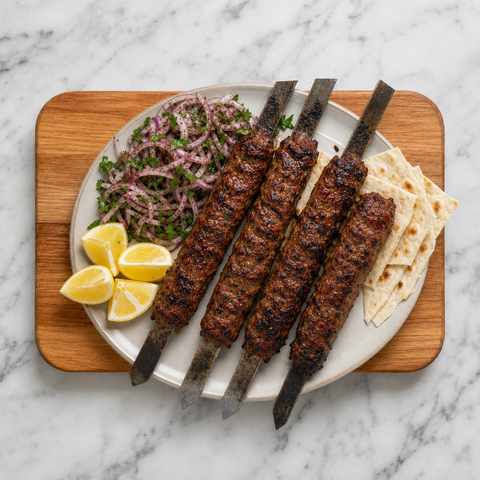 Verkohlte Adana-Kebabs mit Sumach-Zwiebeln, Petersilie, Zitrone und Fladenbrot serviert.