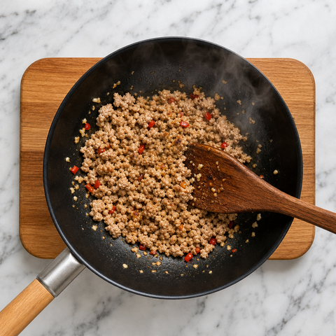 Ground pork browning with garlic and chilies in a wok