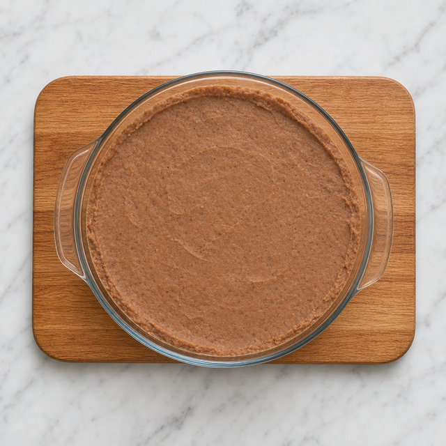 Smooth refried beans spread across the bottom of a shallow serving dish